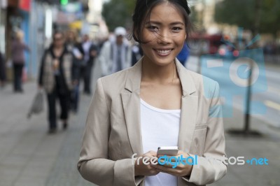 Young Woman And Smart Phone Walking On Street Stock Photo