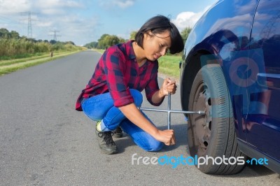 Young Woman Changing Car Wheel On Country Road Stock Photo