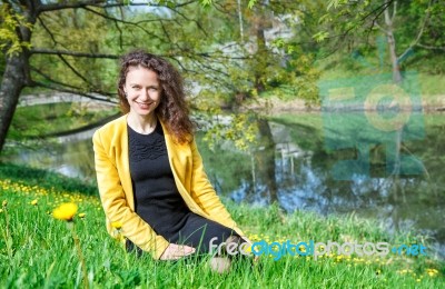 Young Woman Sitting On The Grass Near The Pond Stock Photo