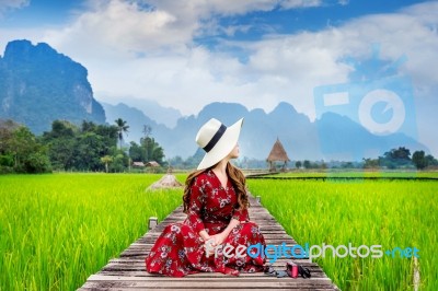 Young Woman Sitting On Wooden Path With Green Rice Field In Vang Vieng, Laos Stock Photo