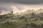 Alpine Village In Mountains. Smoke, Bonfire And Haze Over Hills Stock Photo