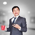 Asian Businessman With Cup Of Coffee And Using Smartphone Looking Away On Blank Space Stock Photo