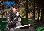 Beautiful Woman Sitting On A Park Bench Holding A Pen And Notebo Stock Photo