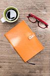 Blank Orange Leather Diary,glasses And A Cup Of Coffee On Wooden Desk Stock Photo