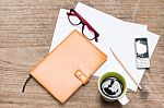 Diary,blank Paper With Pencil, A Cup Of Coffee, Mobile Phone And Eye Glasses On Wood Table Stock Photo