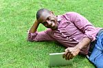 Handsome Man Lying On The Lawn With Tablet Stock Photo