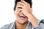 Laughing Young Man With Hand On His Face Stock Photo