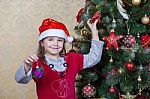 Little Girl In Santa Hat Near Christmas Tree Stock Photo