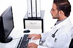 Male Doctor Working With Desktop At His Desk Stock Photo