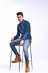 Male Model In Denim Jeans Sitting On A Chair . Studio Shoot Stock Photo