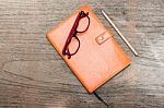 Orange Diary With Pencil And Eye Glasses On Wood Table Stock Photo