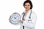 Pretty Doctor Pointing Out Time On Wall Clock Stock Photo