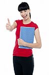 Pretty Teenager Holding Notebook And Gesturing Thumbs Up Stock Photo