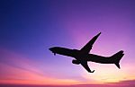 Silhouetted Commercial Airplane Flying At Sunset Stock Photo