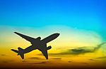 Silhouetted Commercial Airplane Flying At Sunset Stock Photo