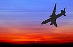 Silhouetted Commercial Airplane Flying At Sunset Stock Photo