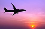 Silhouetted Commercial Airplane Flying At Sunset Stock Photo