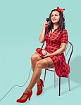 Smiling Young Pinup Woman Sitting On A Chair And Talking On Phon Stock Photo