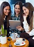 Three Young Woman Using Digital Tablet At Cafe Shop Stock Photo