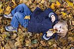 Toddler Blond Boy With Blue Eyes Lays On Bed Of Autumn Fallen Le Stock Photo