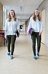 Two Dutch Teenage Girls Walking In Long School Corridor Carrying Stock Photo