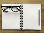 White Paper Note Book With Grey Pencil And Black Glasses On Wood Stock Photo