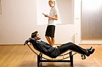 Woman Reading Man Lying On Chaise Longue Stock Photo