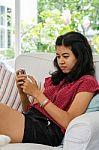 Woman With Her Smart Phone Sitting On Sofa In Living Room Stock Photo