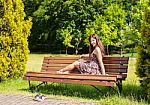 Young Beautiful Brunette Sitting On A Bench In A City Park Stock Photo