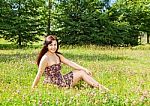 Young Beautiful Brunette Sitting On The Grass Stock Photo