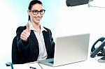 Young Businesswoman Sitting On Desk  Gesturing Thumbs Up Stock Photo