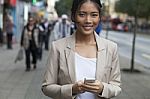 Young Woman And Smart Phone Walking On Street Stock Photo