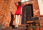 Young Woman In Red Dress Is Standing With Her Back On The Stairs Stock Photo