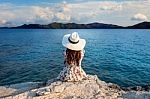 Young Woman Sitting On The Top Of Rock And Looking At The Seashore Stock Photo