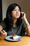 Young Woman Talking Mobile Phone With A Cake In Cafe Stock Photo